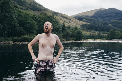 Shirtless man making face while standing in lake