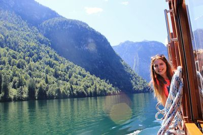 Portrait of smiling young woman in ferry boat on lake against mountains