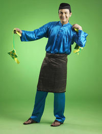 Man in traditional clothing holding decorations against green background
