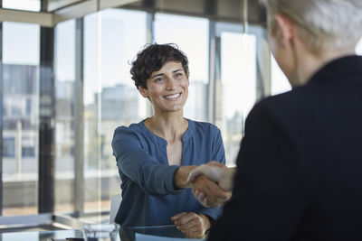 Two businesswomen shaking hands at desk in office