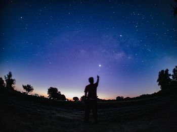 Silhouette man pointing towards star at night