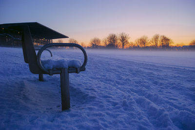 Snow covered field against sky during sunset