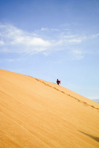 Man on sand dune in desert against sky