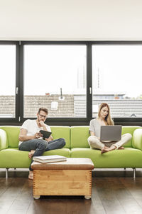 Young couple in living room at home using laptop and tablet