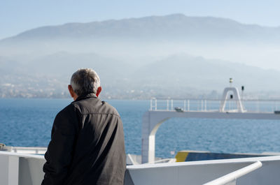 Rear view of man standing on railing against sea