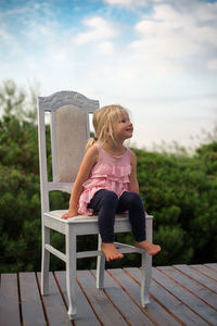 Full length of girl sitting on chair at floorboard