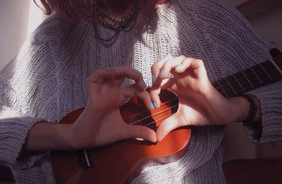 Midsection of woman making heart shape with hands while holding guitar