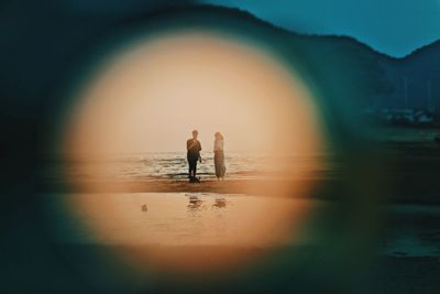 Digital composite of man and woman standing at beach against sky