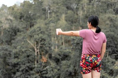 Rear view of woman standing against trees