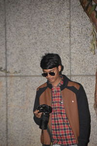 Young man wearing sunglasses standing against wall