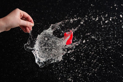 Cropped hand of person exploding water bomb against black background