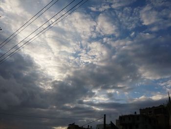 Low angle view of electricity pylon against cloudy sky
