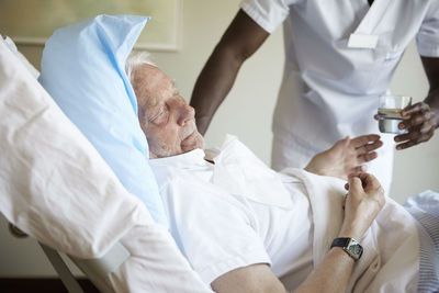 Midsection of male nurse giving drinking water to senior man in hospital ward