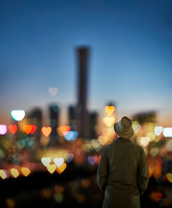 Digital composite of man standing by illuminated heart shapes against sky at night