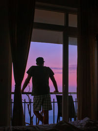 Rear view of silhouette man standing by window