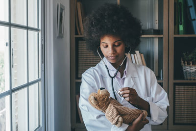 Smiling doctor examining stuffed toy at clinic