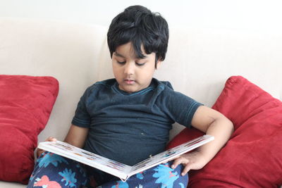 Cute boy reading picture book against white wall at home