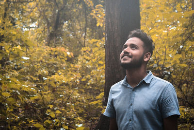 Young man looking up while standing in forest