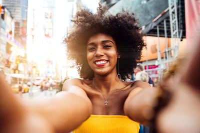 Portrait of happy young woman with afro hairstyle taking selfie on city street