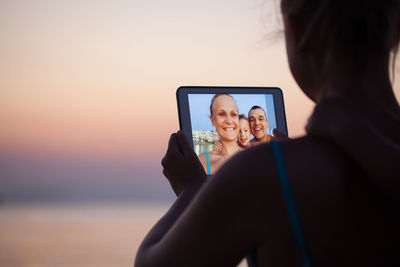 Silhouette of woman using digital tablet in sea at sunset