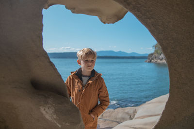 Boy standing on rock at sea against sky