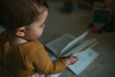 Side view of cute baby girl playing with book at home