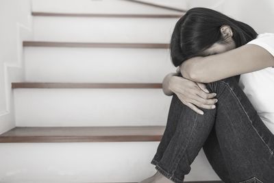 Side view of woman sitting on wall at home