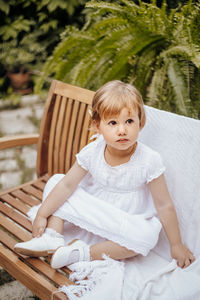 Little blonde girl sits on a wooden bench in the garden. child is wearing a dress. childhood