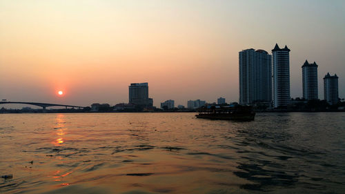 Sea by buildings against sky during sunset