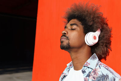 Portrait of young man looking away against orange wall