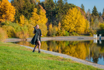 A woman with long hair walks in an autumn park by a pond and throws stones into the water. 