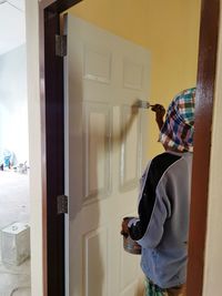 Rear view of man holding glass door at home