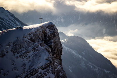 Dramatic scenic view of snowcappedmountain cliff against sky. with summit cross and hut