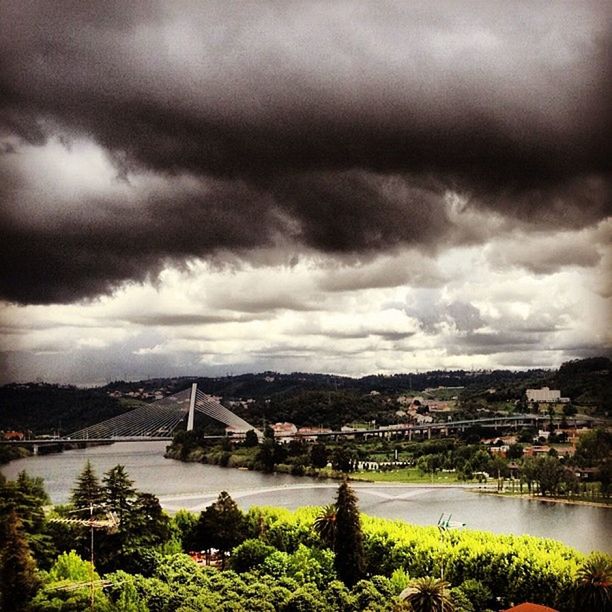 architecture, sky, built structure, cloud - sky, cloudy, water, river, bridge - man made structure, building exterior, city, connection, tree, cityscape, overcast, cloud, weather, bridge, high angle view, nature, outdoors