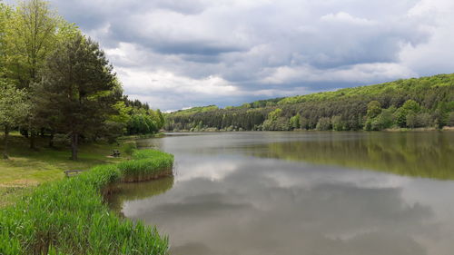 Scenic view of lake and green landscape against cloudy sky