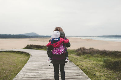 Rear view of mother carrying son wile walking on boardwalk