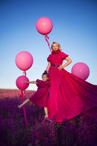 Family mother and daughter in pink dresses are standing in a field with flowers and big balloons