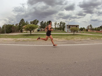 Full length of woman running on road against sky