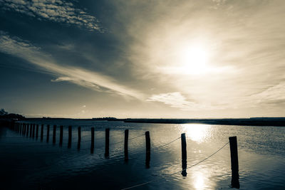 Silhouette wooden posts in lake against sky during sunset