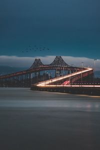 Illuminated bridge over sea against sky in city