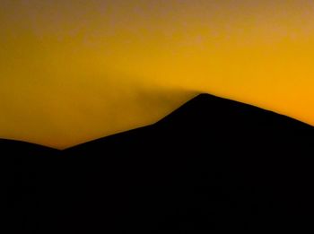 Low angle view of silhouette mountain against orange sky