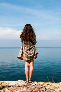 Rear view of young woman standing by sea against sky