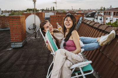 Cheerful women enjoying while sitting on chair at rooftop