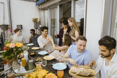 Group of male and female multiracial friends having food and drinks at dinner party in balcony