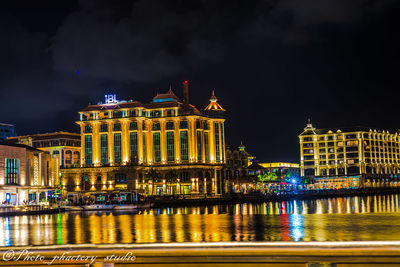 Illuminated building by river against sky at night