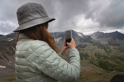 Woman takes a picture on the phone while standing on top of a hill. portrait of a tourist in the