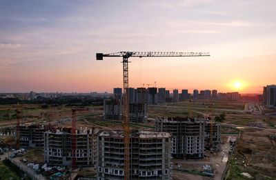 Crane by building against sky during sunset