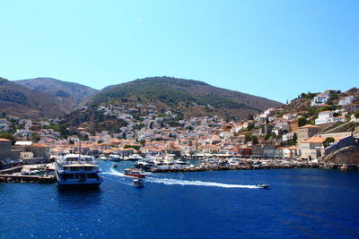 Boats moored in sea by town against clear blue sky