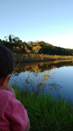 Rear view of girl by lake against clear sky