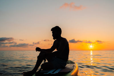 Side view of silhouette man standing at sea against sky during sunset